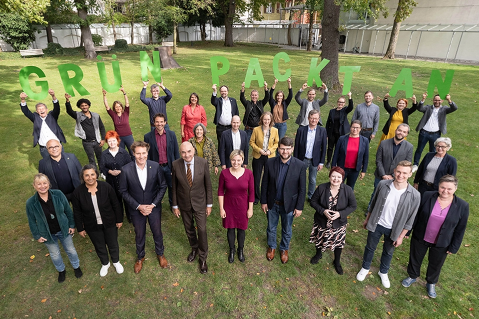 Blog | Voller Elan in die neue Wahlperiode Gruppenfoto der neuen Abgeordneten der Grünen-Fraktion im Bayerischen Landtag, aufgenommen im Freien. Die Personen stehen auf einer Wiese und halten große grüne Buchstaben mit dem Schriftzug „GRÜN PACKT AN“.